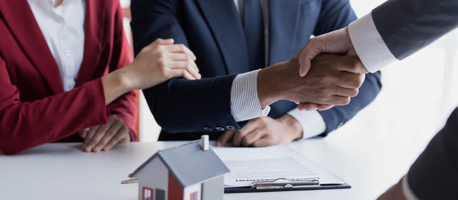 Happy couple first time home owners handshaking realtor insurer landlord bank worker at meeting