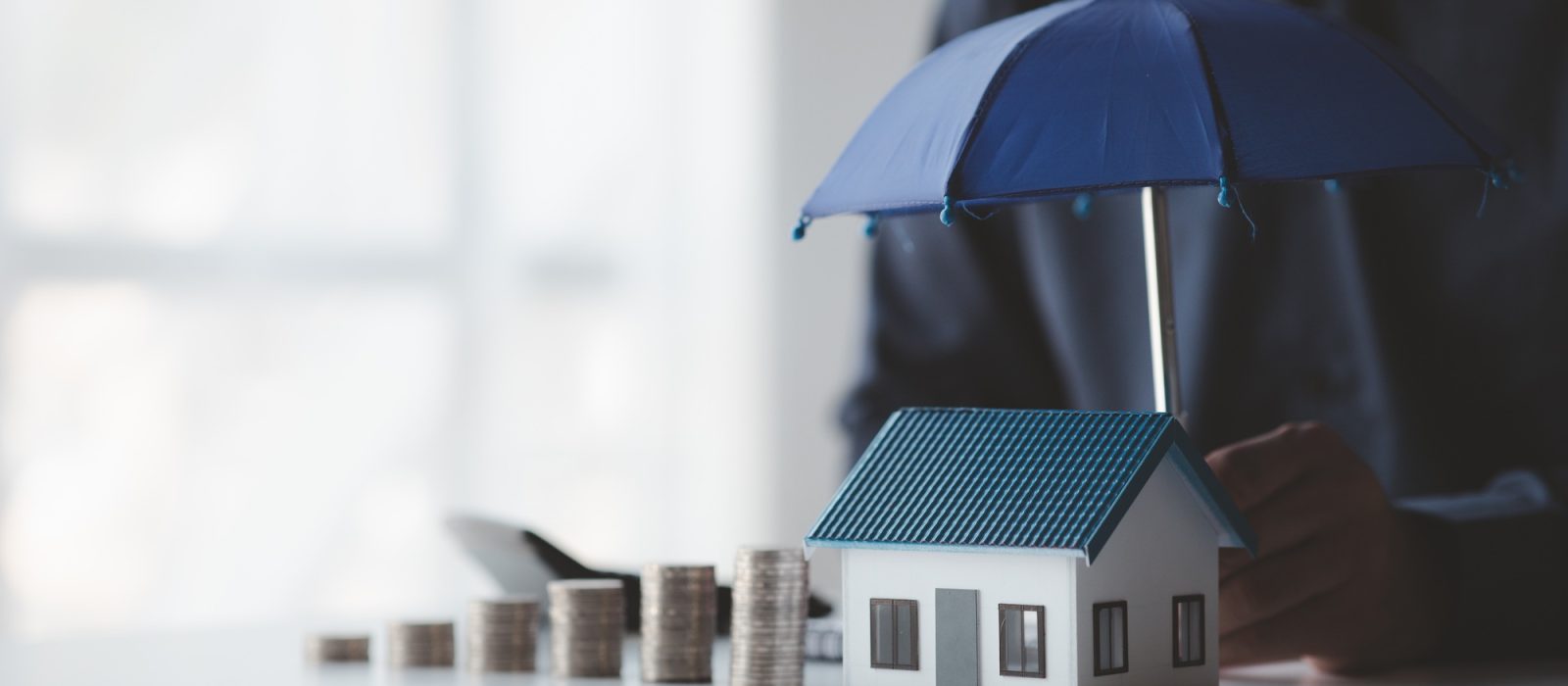 Individuals holding small umbrellas and model homes, housing insurance against impending loss and fi