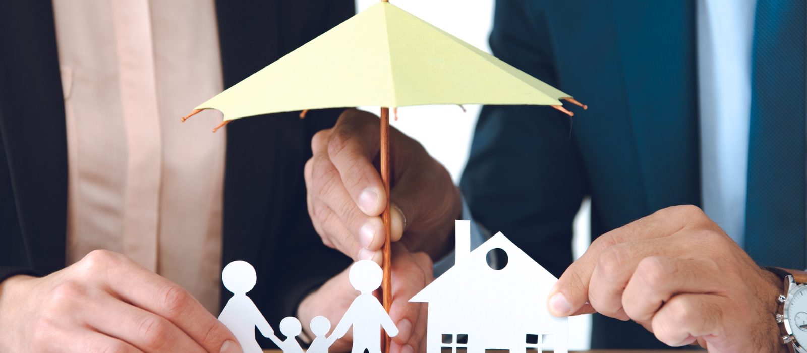 partial view of insurance agents covering family and house paper models with umbrella at workplace