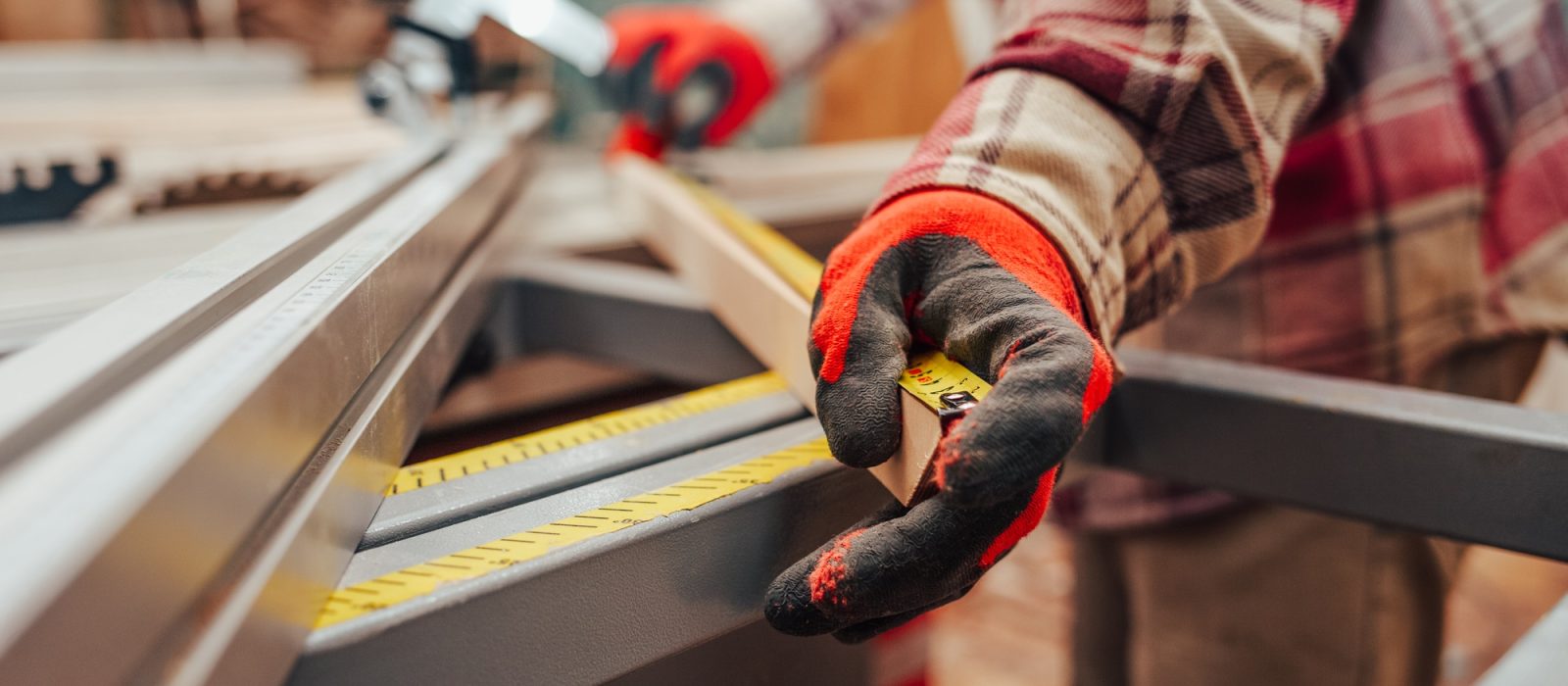 Worker in a carpentry shop measures plywood for cutting